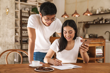 Image of smiling couple using cellphone and making notes in planner