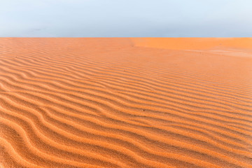 Orange sand lies beautifully in waves at sunset. Sand texture close-up. Hills of yellow sand in Vietnam.