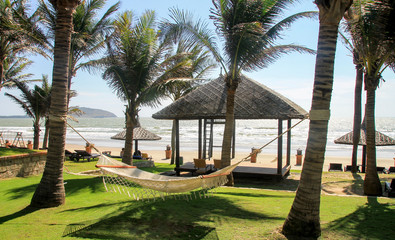 On the seashore, on the beach, a hammock hangs on two palm trees. Relaxing holiday on a Sunny day under the shade of trees and a refreshing breeze from the sea.
