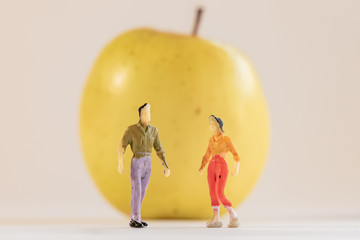 Miniature woman and man figure standing next to big yellow apple. Shallow depth of field background. Healthcare, healthy lifestyles and slimming concept.