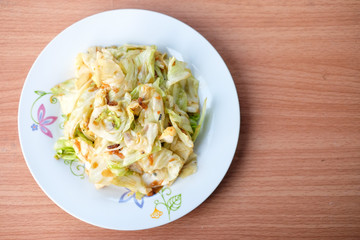 The hot stir fried cabbage with fish sauce serve on white dish set on brown table - homemade food concept.