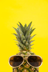 Summertime pineapple fruit with sunglasses against a bright yellow background