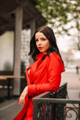 
Beautiful young, sexy woman with red lips in a red cloak, dressed on her naked body, open neckline, chest after plastic surgery, beautiful breasts 3 sizes, against the black walls, in the city