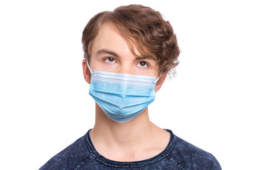 Concept of coronavirus quarantine. Child Teen boy wearing medical face mask to health protection from influenza virus, isolated on white. COVID-19 - home self isolation. Emotional portrait of teenager