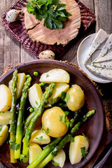 Boiled potato with grilled green asparagus on brown plate over on old wooden background.