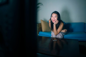 young happy and beautiful Asian Korean woman watching TV  at living room sofa couch enjoying funny...