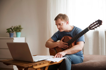 Man playing acoustic guitar and watching online lesson on laptop while practicing at home. Stay home. quarantine. Online training, online classes.
