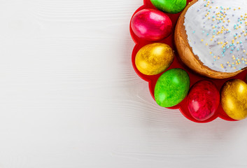 Easter cake kulich. Traditional Easter sweet bread and easter colorful eggs on plate on white wooden background. Copy space.