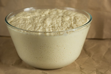 Glass bowl with aired yeast raised dough on paper background