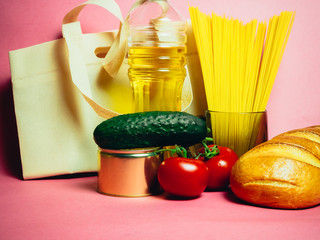 Paper bag with Food supplies crisis food stock for quarantine isolation period on pink. Vermicelli, pasta, canned food, bananas, butter, bread. Food Delivery, Donation, Coronavirus Quarantine.