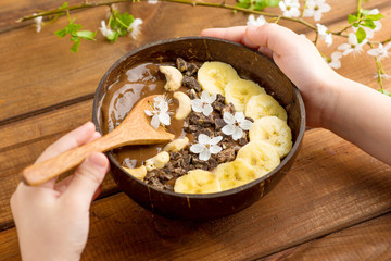 chocolate smoothie with banana and cashew in a coconut bowl and a bamboo spoon