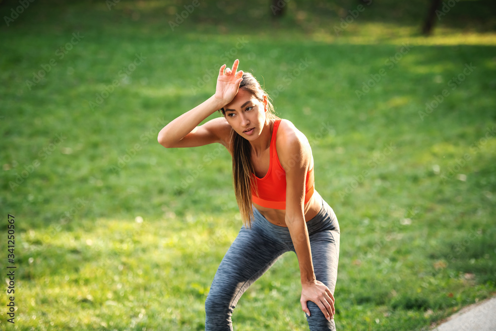 Wall mural young gorgeous fit tired sportswoman taking a break after running and wiping sweat.