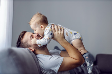 Adorable little blond boy playing with his caring father and biting his nose. Father is smiling.