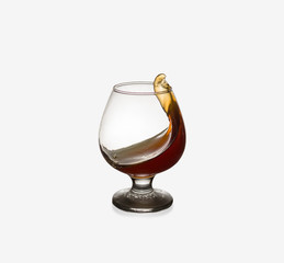 Glass glass with an alcoholic drink or cognac and splashes on a light background. Isolated, splash.