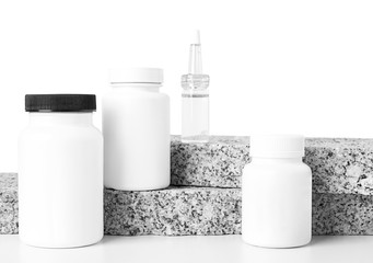  Four different white medical bottles with pills, drops, capsules on two granite tiles on a white background. Health care. Copy space.