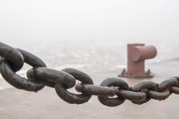 Fototapeta premium Foggy morning on the embankment. A pier on the pier for mooring cable and an iron chain.