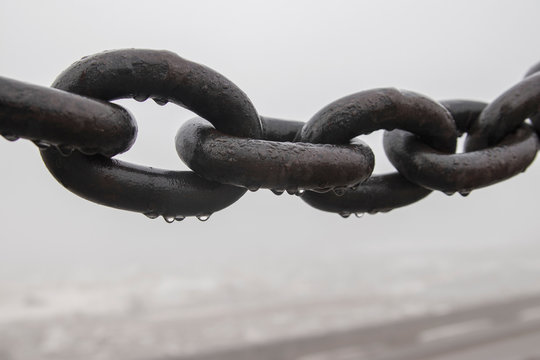 An iron chain on the waterfront on a cloudy, foggy morning, covered with drops of water.