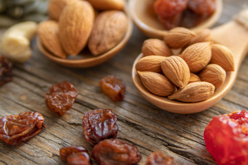 Almonds, apricot seed on a wooden spoons. Raisins, cashews, figs, nuts on top of a wooden board.