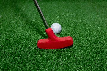 Mini golf. A golf club, red, directs a white ball to move in a given direction.