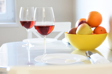 Fruit oranges and apples in a bowl and glasses with wine in a white bright room.