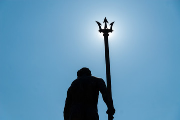 Neptune statue with trident covering the sun - obrazy, fototapety, plakaty