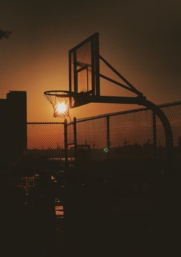 Optical Illusion Of Sun In Basketball Hoop At Court Against Sky During Sunset