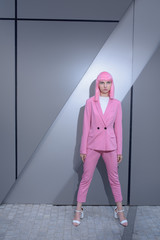 Young woman in pink pant suit with pink hair on metallic, business centre wall background. Conceptual fashion photography. Copy space