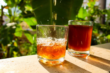 Outdoor Tea pouring into glass cup transparent with day sunlight.
