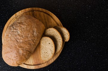 Top view of wooden cutting board and delicious crusty rye bread and slices of it, black kitchen table.Empty space