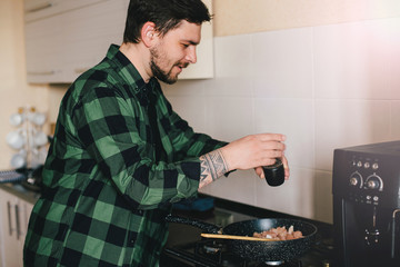 Young man with beard cooking dinner at the kitchen.