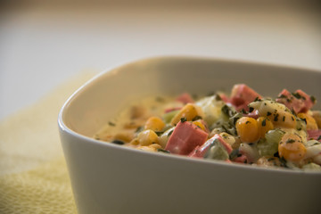 Delicious fresh vegetable salad. Sliced ​​sausage with tender corn. A light table, a beautiful plate and napkins.