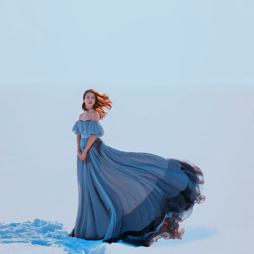Fantasy beauty woman princess. Snow queen stands blue luxury vintage silk fabric dress fluttering in motion. Winter nature white snow. Loose red haired long hair flying in wind. lady medieval clothes