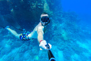 A guy with a mask and snorkel dives into the blue water of the Red Sea and photographs himself