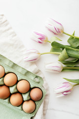 Obraz na płótnie Canvas Easter eggs in a green carton and tulips flatlay