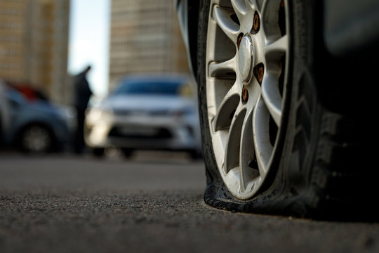 Car tire with a flat tire in the yard near a multi-storey building. Image of an accident, damage, breakdown for illustration on the topic of repair, insurance. Blurred