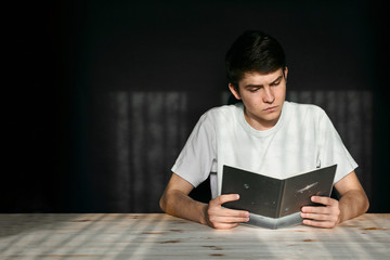 guy in a white T-shirt at a table on a black background reads a notebook