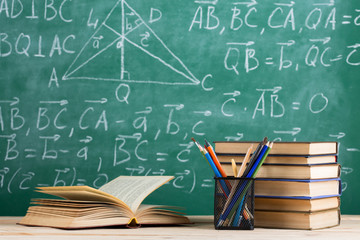 Education and sciences concept - books on the teacher desk in the auditorium, chalkboard on the background.