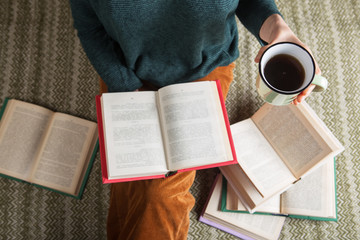 Stay home - Young woman is sitting on a carpet and reading a book, holding a cup of tea