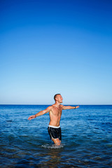 Fototapeta na wymiar Happy man guy joy on vacation, stands at sea and splashes in the water. Men's shorts, sun, beach