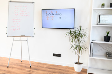Flip chart, monitor screen on the white wall in cozy interior. No people