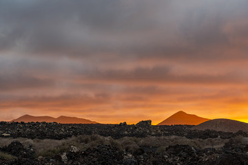 Fototapeta na wymiar Orange sky at sunset in the volcanic park Timanfaya on the island of Lanzarotte in Spain 