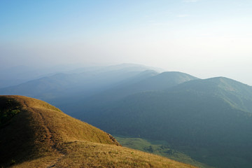 Natural landscape of grassy pathway to the mountain peak with cloudy blue sky