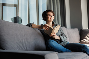 Image of brunette cute pleased woman reading book and smiling