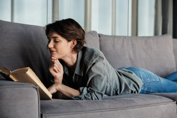 Image of brunette cute pleased woman reading book and smiling