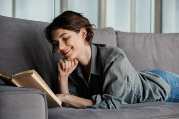 Fototapeta premium Image of brunette cute pleased woman reading book and smiling