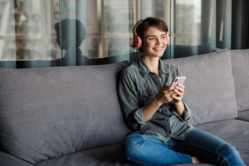 Image of nice young smiling woman using smartphone and headphones
