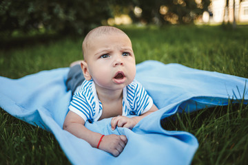 Little boy 3 months old lies on his stomach on a blue bedspread in the park around the green grass and trees. Children's emotions of joy