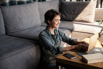 Image of nice young cheerful woman using laptop and smiling