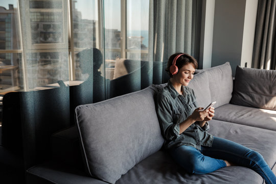 Image of nice young smiling woman using smartphone and headphones