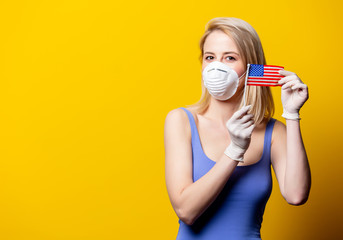 Blonde woman in face mask and gloves holds USA flag on yellow background